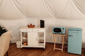 A kitchenette with a microwave, a Galanz refrigerator, a white cabinet with drawers, and a wicker basket on a wooden stand.
