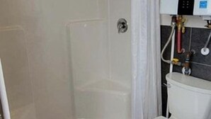 Un baño con ducha, inodoro y un armario blanco con calentador de agua.
