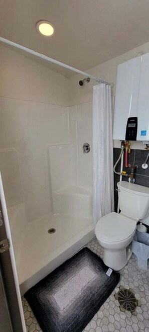 A bathroom with a shower, toilet, and a white cabinet with a water heater.