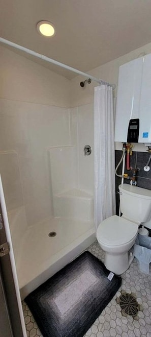 Et badeværelse med bruser, toilet og et hvidt skab med varmtvandsbeholder.