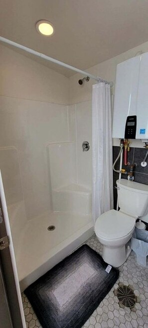A bathroom with a shower, toilet, and a white cabinet with a water heater.