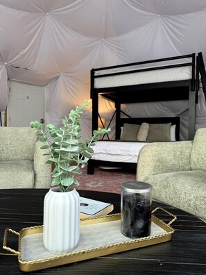 A bunk bed, a white vase with green leaves, and a candle on a tray in a tented room.