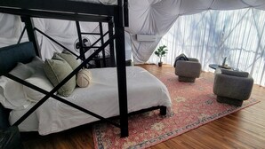 Una habitación con tienda de campaña, una cama con dosel, dos sillones, una mesita y una planta en maceta.