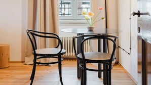 A cozy dining area with a table and chairs, a window with curtains, and a radiator. - Orto Room (Paladina)