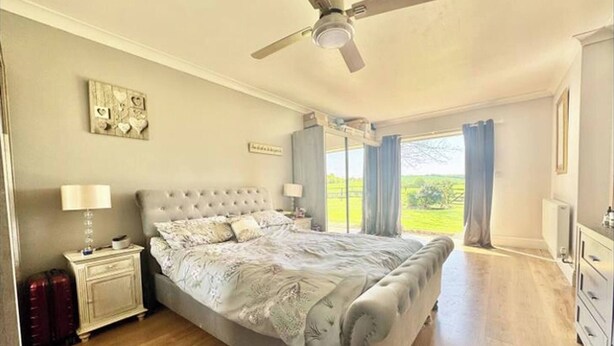 A bedroom with a large bed, a ceiling fan, a nightstand with a lamp, and a view of the outdoors. - The Old Police House (Louth)