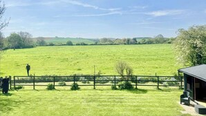 A grassy field with a wooden fence and a building with a dark roof. - The Old Police House (Louth)
