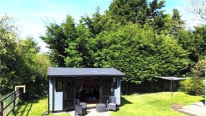 A small, enclosed outdoor seating area with a table and chairs, surrounded by a well-maintained lawn and dense trees. - The Old Police House (Louth)