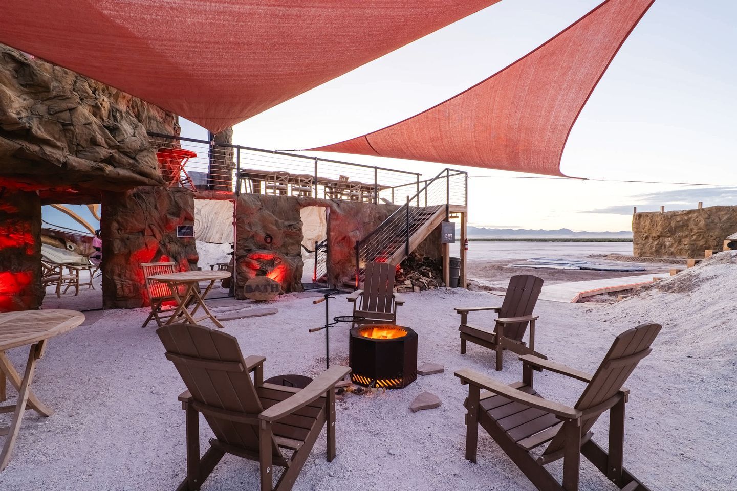 Ein Außenbereich mit Adirondack-Stühlen, einer Feuerstelle und Blick auf den Strand.