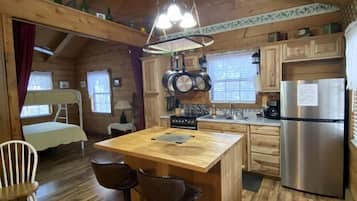 A cabin-style kitchen with a wooden island, bar stools, a refrigerator, and a hanging light fixture.