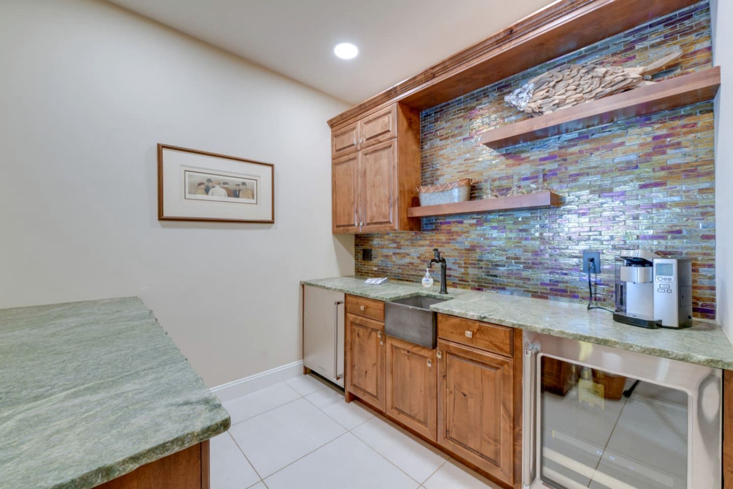 A kitchen with wooden cabinets, a tiled backsplash, a sink, a coffee machine, and a framed picture on the wall.