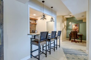 A dining area with a table and chairs, a hanging light fixture, and a painting on the wall.