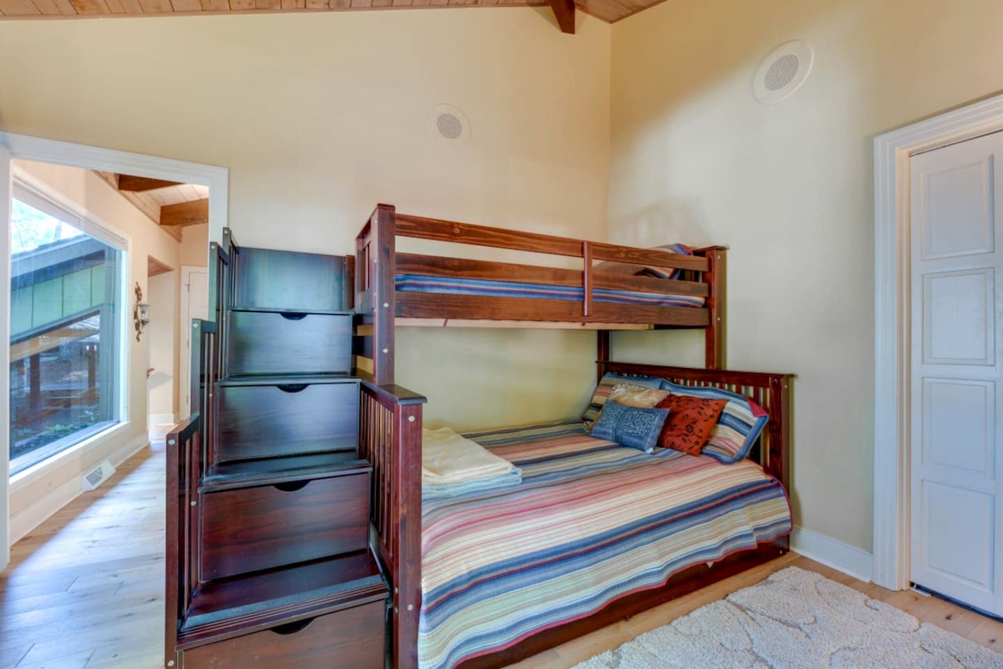 Uma cama beliche com gavetas, uma janela e uma porta.