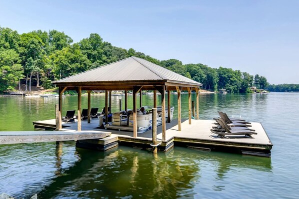 Ein Pavillon mit Dach, ein Steg und Liegestühle an einem See.