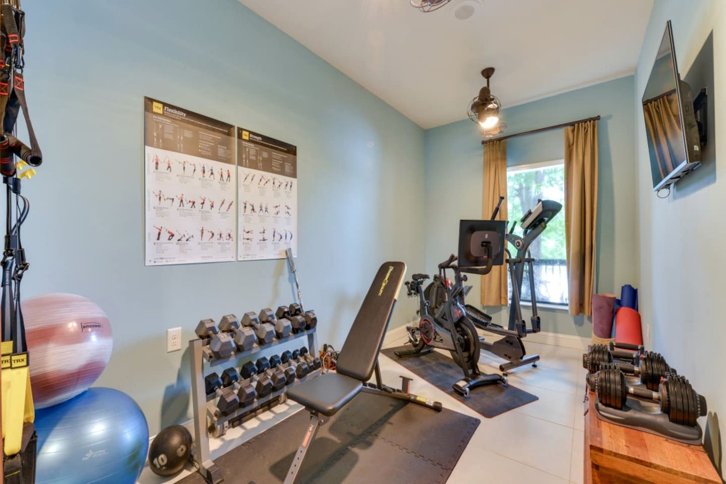 Uma academia em casa com equipamentos de ginástica, uma máquina de remo, halteres e bolas de exercícios.