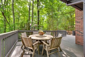 Eine Holzterrasse mit einem runden Tisch und Stühlen, umgeben von einem Wald.