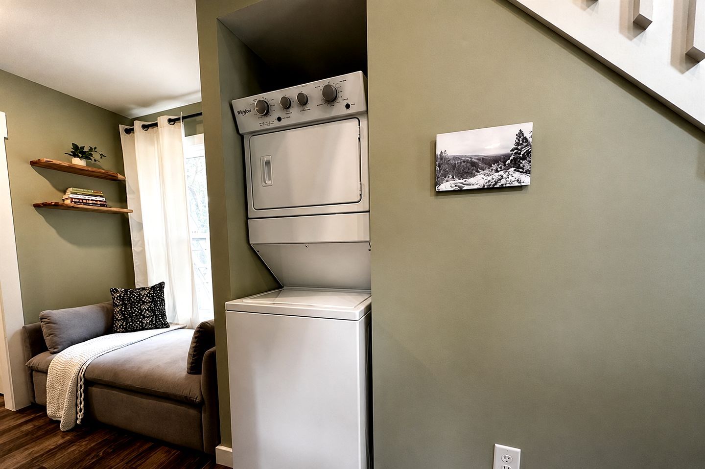 A compact living space with a bed, a small sofa, a washing machine, and a shelf with books.