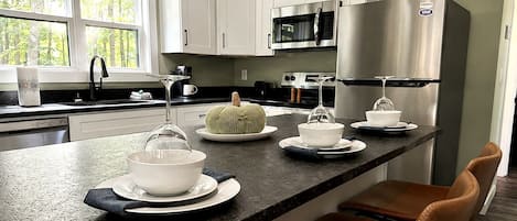 Cozinha moderna com armários brancos, eletrodomésticos de aço inoxidável e uma ilha central com banquetas.