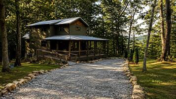 A cabin with a porch, surrounded by trees and a gravel driveway.
