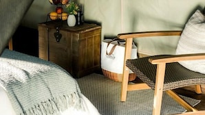 Une pièce aménagée avec une tente, un lit, une chaise, une petite malle en bois et une fenêtre donnant sur la forêt.