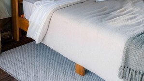 Un lit avec une tête de lit en bois, plusieurs oreillers, un couvre-lit blanc et un tapis à motifs.