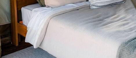 A bed with a wooden headboard, multiple pillows, a white bedspread, and a patterned rug.