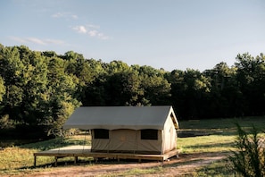 A single-room tent with a flat roof, a bench outside, and a forested background.
