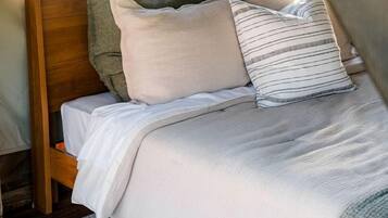 A bed with a wooden headboard, multiple pillows, a white bedspread, and a patterned rug.
