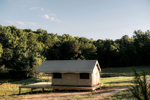 A single-room tent with a flat roof, a bench outside, and a forested background.