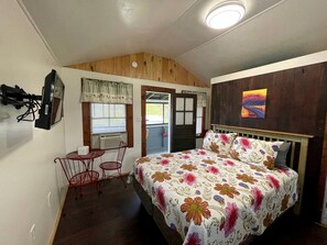 A bedroom with a bed, a small table, a chair, a door, and a window. - Lakefront Secluded Cottage in Northwood, New Hampshire (Northwood)