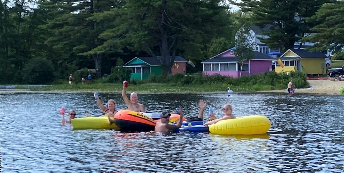 Människor som flyter på vattnet i en naturskön miljö, med hus i bakgrunden.