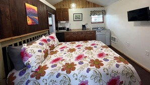 Quarto com cama, escrivaninha, cadeira, janela e um espaço de cozinha.