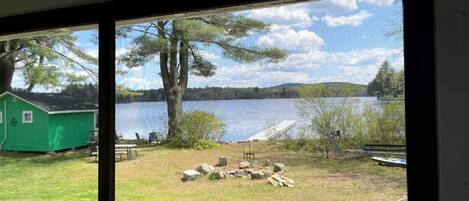 A view of a lake with a green shed and a fire pit area.