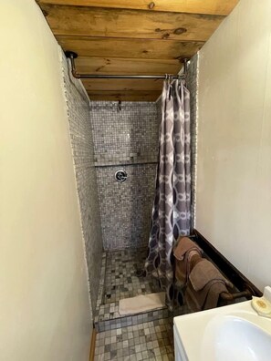 A small bathroom with a shower, tiled floor, wooden ceiling, and a towel rack. - Lakefront Secluded Cottage in Northwood, New Hampshire (Northwood)