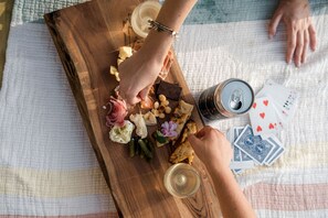 A wooden board with various food items and a can of beer, a glass of wine, and playing cards on a table. - Tranquil Tented Cabin with Lake Views in South Carolina (Greenville)