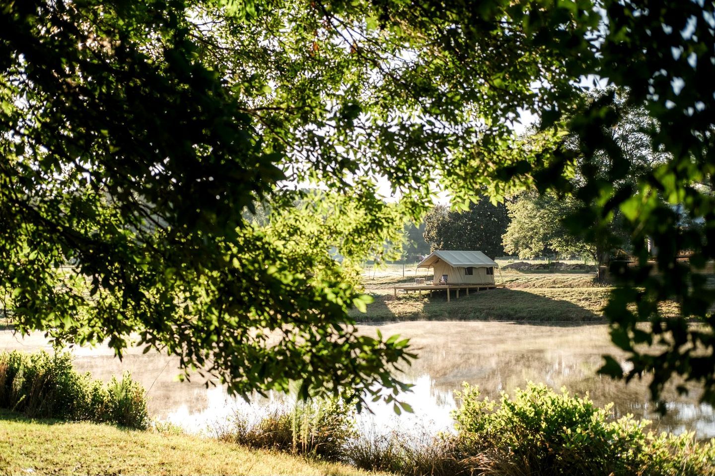 Ein Zelthaus am Wasserufer, umgeben von Bäumen und Gras.