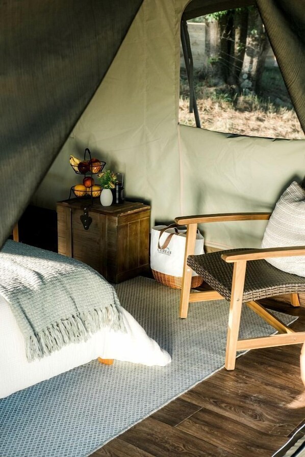 A tented room with a bed, a chair, a small wooden chest, and a window with a view of trees.