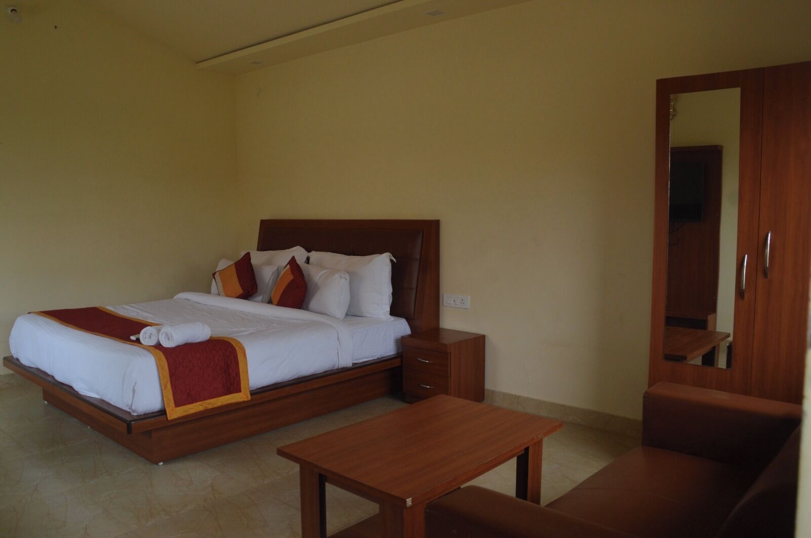 A neatly made bed with a wooden headboard, a bedside table, and a wardrobe with a mirror.