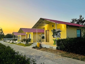 A row of yellow brick buildings with red roofs, each with a small porch and a door. - S K Pushkar Resort (Peesangan)