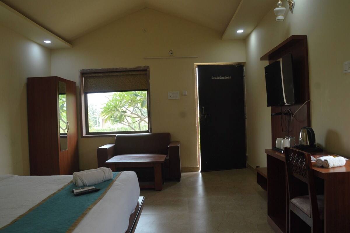 A hotel room with a bed, a desk with a chair, a television, and a door.