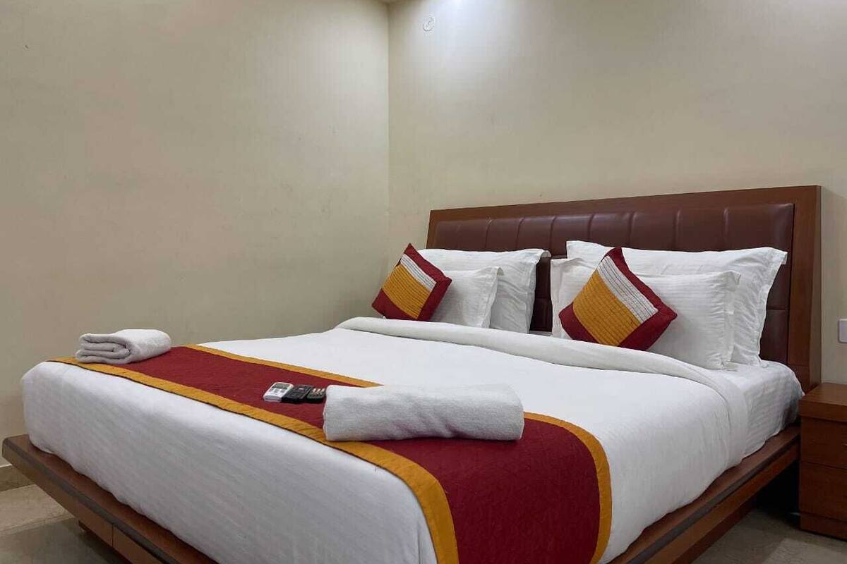 A neatly made bed with white linens and red accents, a remote control, and a folded towel on the bed.