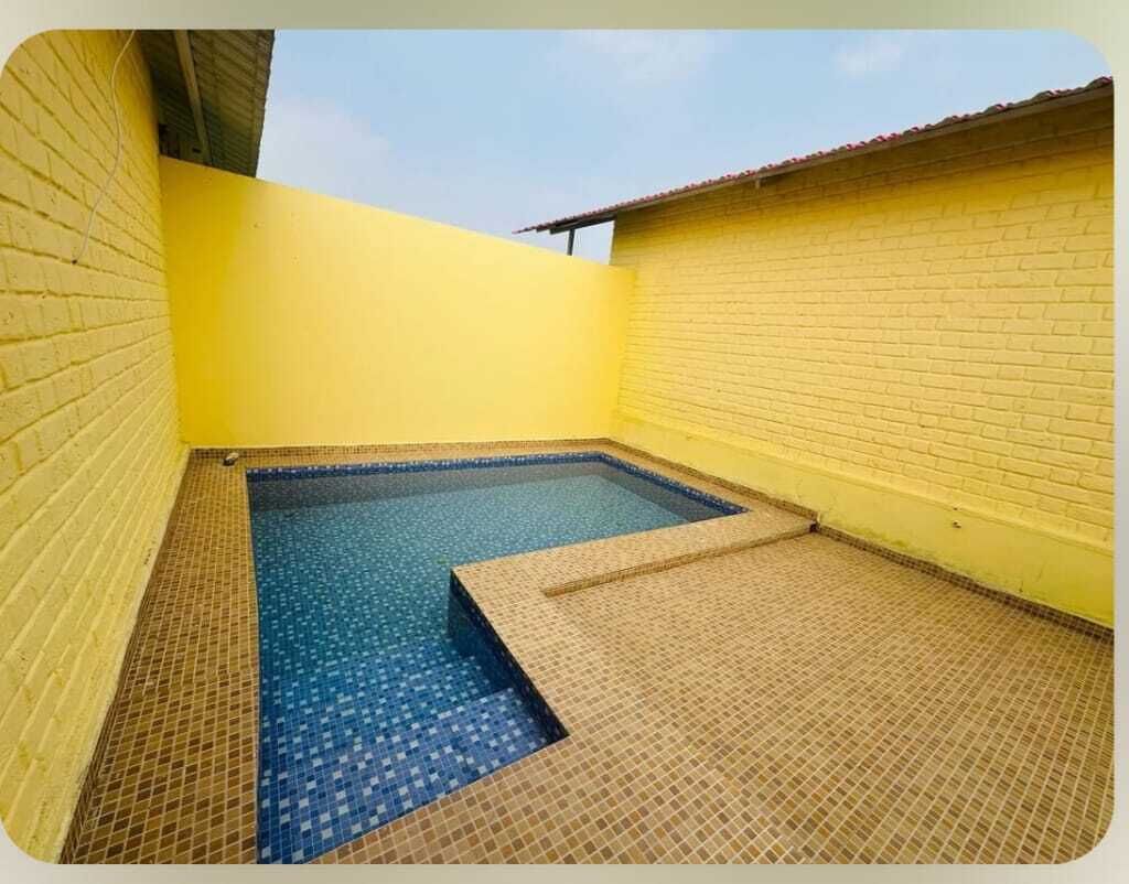 Una piscina pequeña al aire libre con suelo y paredes de azulejos, rodeada de muros de ladrillo amarillo.