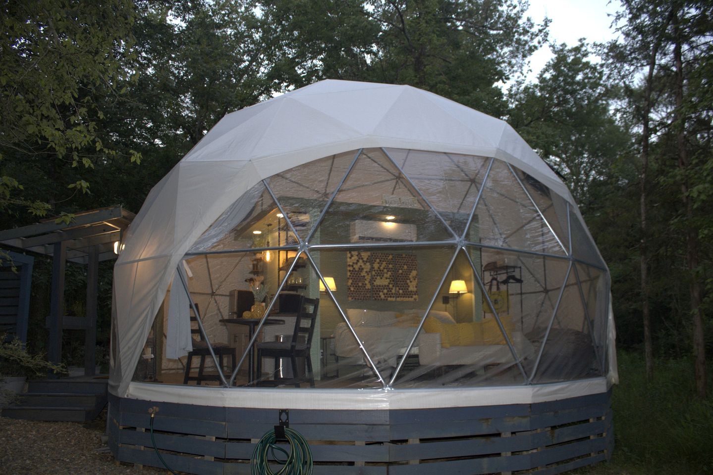 A geodesic dome structure with a transparent roof, revealing an interior with a dining area and seating.