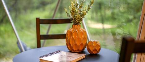 Ett runt bord med ett spiralformat anteckningsblock, en dekorativ orange vas med en växt och en mindre orange vas med en sfärisk design.