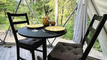 Un comedor con una mesa y sillas, un florero y una botella, con árboles de fondo.