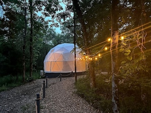 A geodesic dome structure in a forested area with a gravel path leading to it.