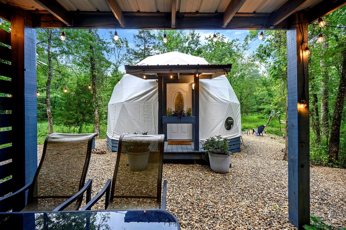 A cozy outdoor seating area with a covered structure, a wooden deck, and a gravel path leading to a tent.