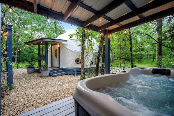 A hot tub, a covered outdoor seating area, and a tent-like structure in a forested setting.