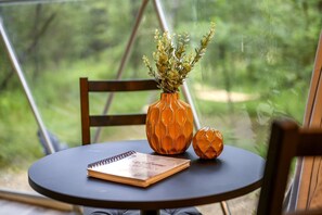 A round table with a spiral notebook, a decorative orange vase with a plant, and a smaller orange vase with a spherical design.
