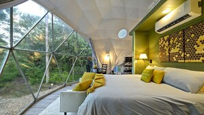 Habitació tipus tenda moderna amb un llit gran, zona de seients i vistes al bosc.