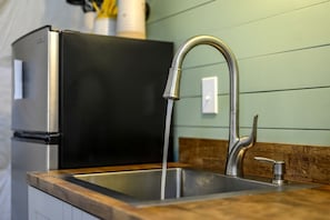 A kitchen with a stainless steel sink, a modern faucet, and a black refrigerator.